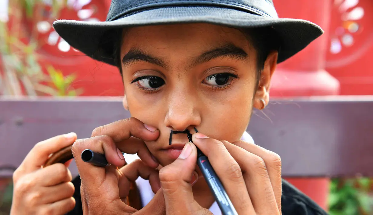 Seorang anak dirias selama memperingati ulang tahun Charlie Chaplin di Adipur, India (16/4). Ratusan pengemar Charlie Chaplin mengenakan topi bowler dan kumis palsu membawa tongkat berjalan merayakan aktor komik tersebut. (AFP Photo/Indranil Mukherjee)