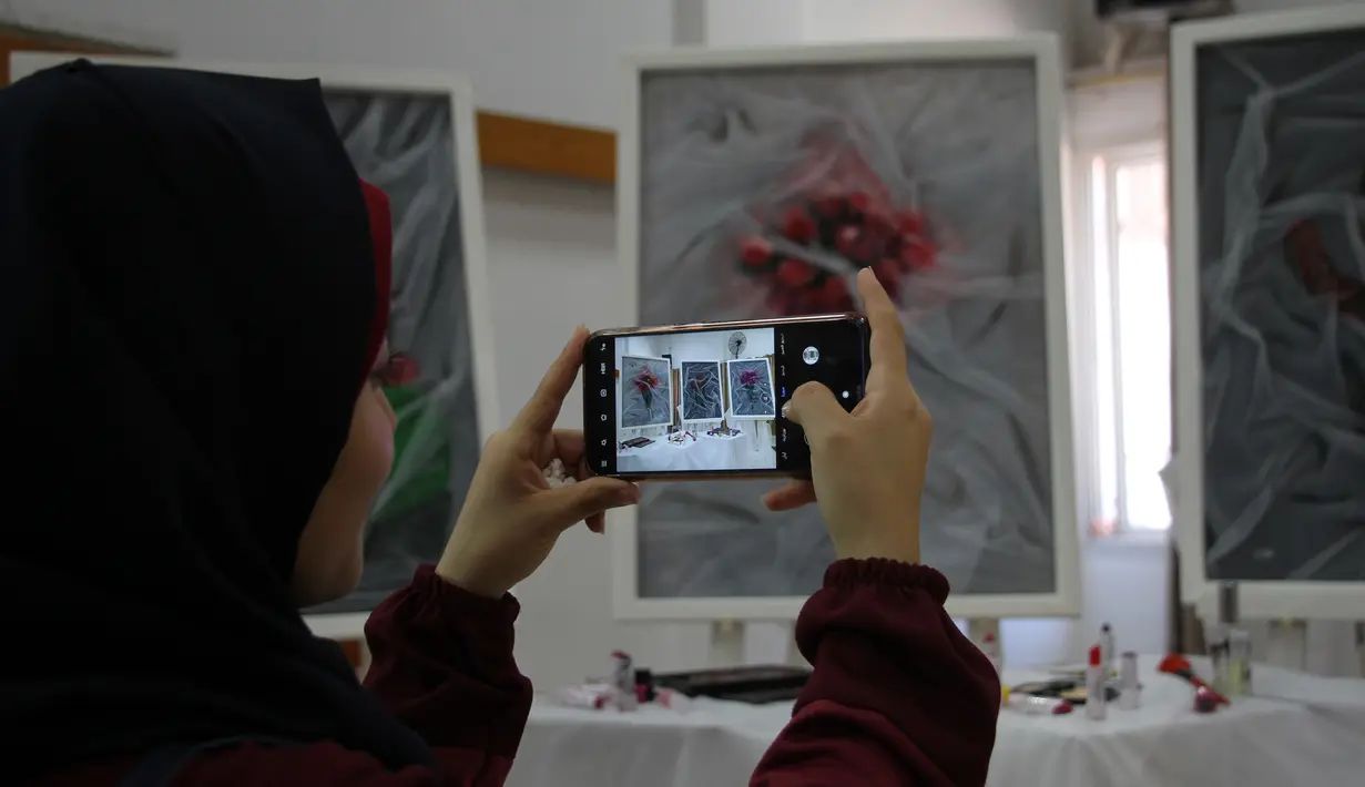 Seorang perempuan memotret karya seni di pameran seniman Palestina Kholoud al-Dasooqi di Gaza City, 11 Agustus 2020. Seniman asal Kota Khan Younis di Jalur Gaza itu menggelar pameran selama dua hari untuk mengungkap kekerasan terhadap perempuan melalui puluhan lukisan. (Xinhua/Rizek Abdeljawad)