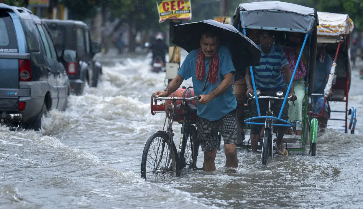 Seorang pria membawa tabung gas di sepedanya dan menyeberangi jalan yang banjir saat hujan deras di Guwahati, negara bagian Assam, India, Kamis (16/6/2022). Pemerintah Assam telah memerintahkan penutupan semua institusi pendidikan di Guwahati karena peringatan siaga merah untuk hujan lebat. (AP Photo/Anupam Nath)