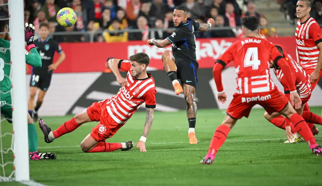 Pemain Atletico Madrid Memphis Depay (tengah) menantang kiper Girona Paulo Gazzaniga pada pertandingan sepak bola Liga Spanyol di Stadion Montilivi, Girona, Spanyol, 13 Maret 2023. Gol tunggal Alvaro Morata membawa Atletico Madrid mengalahkan Girona. (LLUIS GENE/AFP)