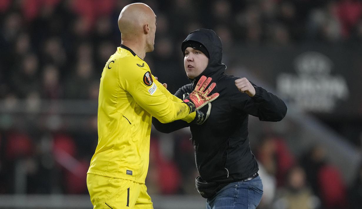 <p>Seorang suporter fanatik PSV berusaha menyerang kiper Sevilla, Marko Dmitrovic dalam laga leg kedua babak playoff fase gugur Liga Europa 2022/2023 di Philips Stadium, Eindhoven, Jumat (24/2/2023). (AP Photo/Peter Dejong)</p>