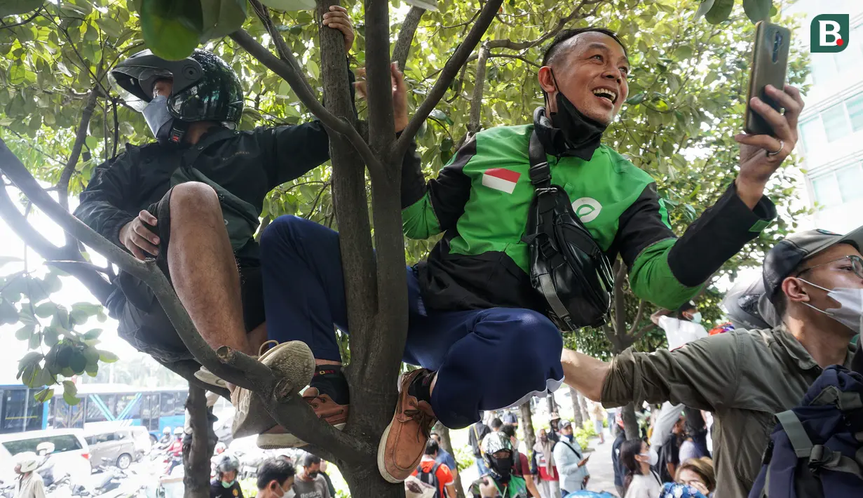 Dua warga memanjat pohon di depan Hotel Kempinski saat mengabadikan parade pembalap MotoGP, Moto2, Moto3, ATC, dan klub motor dari Istana Merdeka hingga Hotel Kempinski di Bundaran HI Jakarta Pusat, Rabu (16/03/2022). (Bola.com/Bagaskara Lazuardi)