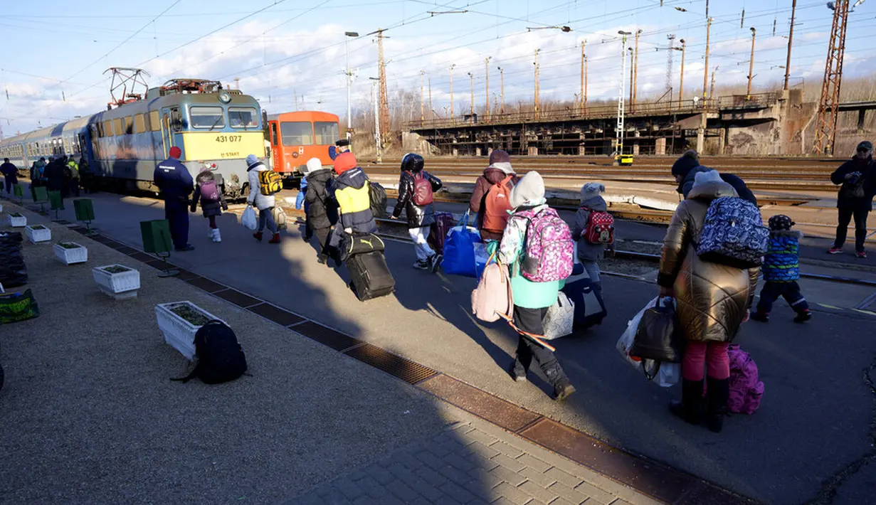 Orang-orang membawa barang-barang mereka saat berjalan untuk mengejar kereta api ke Budapest di stasiun di Zahony, Hungaria, 8 Maret 2022. PBB mengatakan, serangan gencar Rusia telah memaksa lebih dari 2 juta orang meninggalkan Ukraina. (AP Photo/Darko Vojinovic)