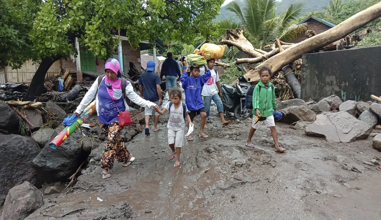 Orang-orang berjalan di tengah puing-puing di sebuah desa yang terkena banjir di Ile Ape, di Pulau Lembata, provinsi Nusa Tenggara Timur, Minggu (4/5/2021).  sejumlah ruas jalan dan jembatan rusak akibat banjir bandang tersebut. . (AP Photo/Ricko Wawo)