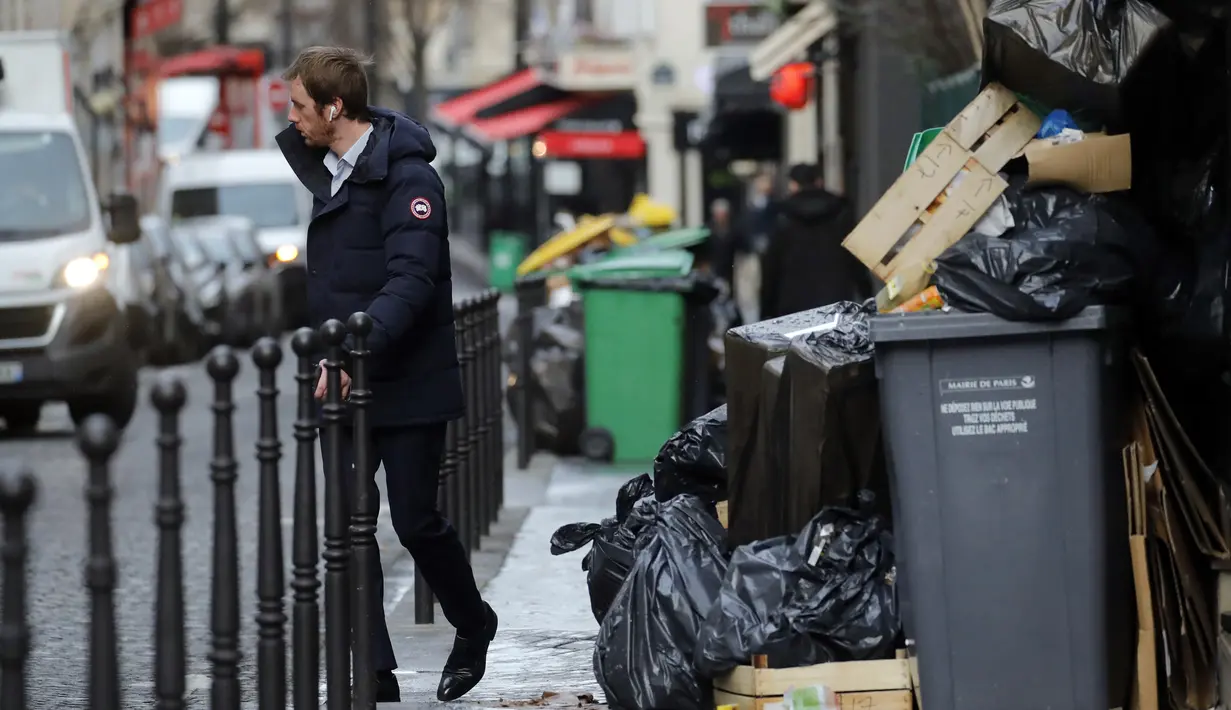 Seorang pria berjalan melewati tong sampah di Paris (4/2/2020). Serikat pekerja memutuskan kegiatan di pabrik pembakaran kunci untuk memprotes reformasi yang mereka katakan tidak adil. (AP Photo/Christophe Ena)