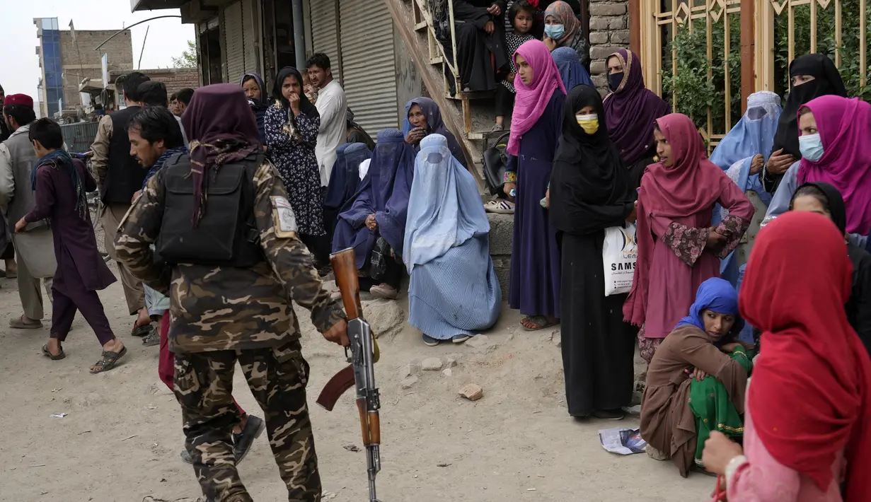 <p>Seorang Taliban berdiri di antara orang-orang yang menunggu untuk menerima jatah makanan yang didistribusikan oleh kelompok bantuan kemanusiaan Korea Selatan, di Kabul, Afghanistan, Selasa (10/5/2022). Taliban pada Sabtu pekan lalu memerintahkan semua perempuan Afghanistan menutupi seluruh tubuhnya atau mengenakan burqa tradisional di depan umum. (AP Photo/Ebrahim Noroozi)</p>