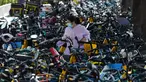 Seorang wanita berjalan melintasi sepeda-sepeda yang diparkir di atas trotoar di Beijing, China (21/7/2020). Seperti diketahui Beijing telah menerapkan bike sharing yang sudah tersedia di trotoar-trotoar Kota Beijing. (AFP Photo/Greg Baker)