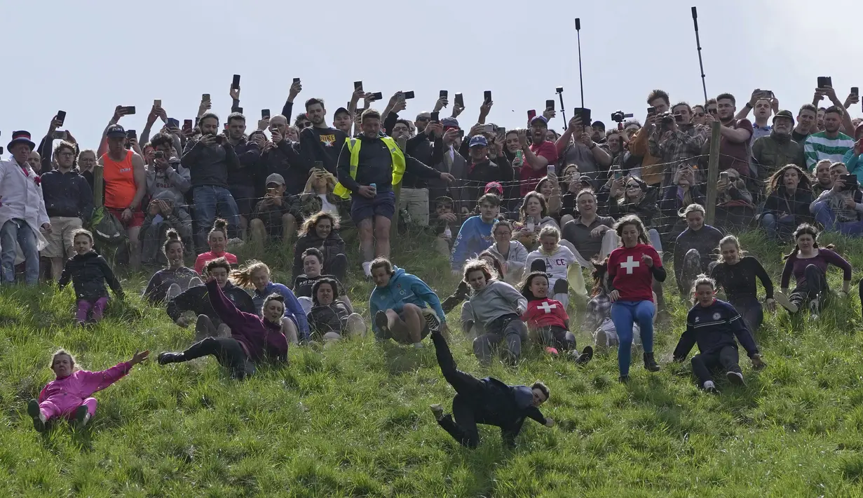 Para peserta bersaing dalam perlombaan menuruni bukit putri selama kontes Cheese Rolling di Cooper's Hill di Brockworth, Gloucestershire, Senin 29 Mei 2023. (AP Photo/Kin Cheung)