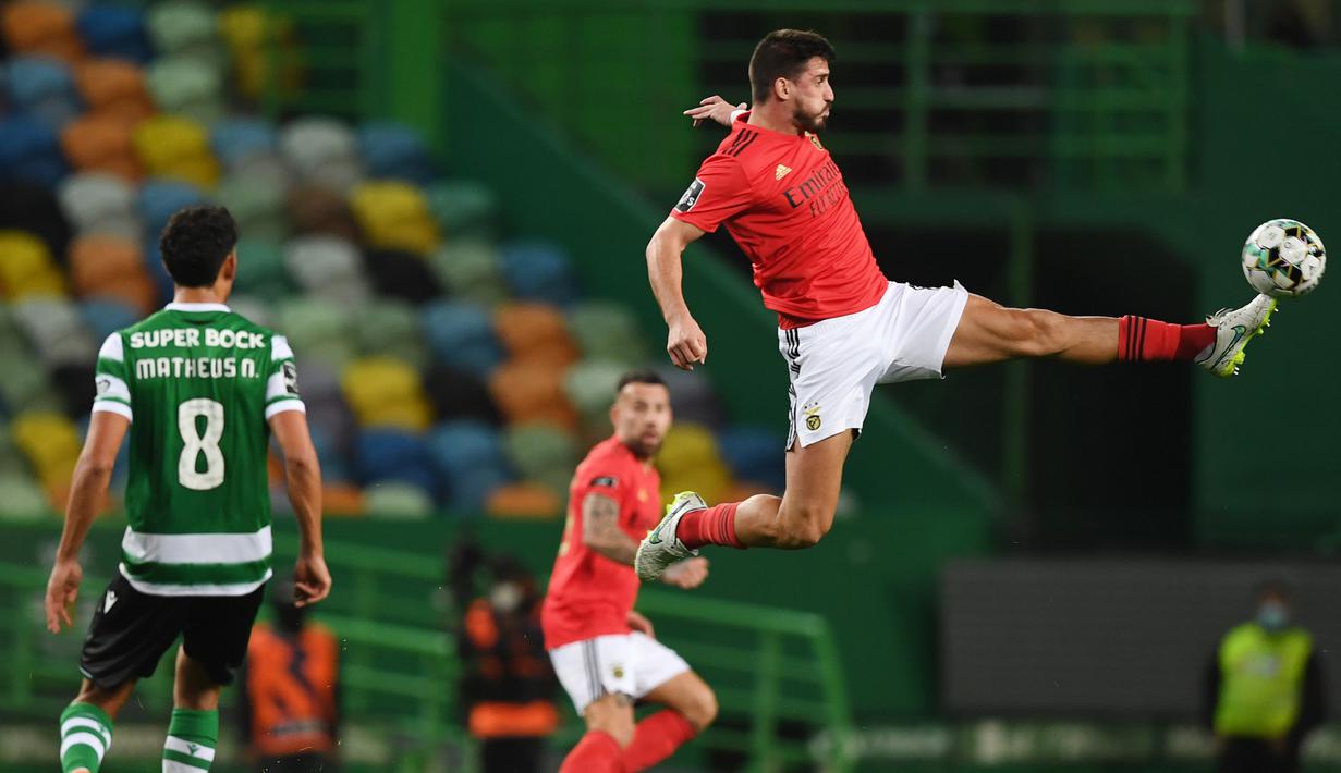 Gelandang Benfica, Gabriel (kanan) menendang bola sambil melompat dalam laga lanjutan Liga Portugal 2020/21 melawan Sporting Lisbon di Jose Avalade Stadium, Lisbon, Senin (1/2/20201). Benfica kalah 0-1 dari Sporting. (AFP/Patricia De Melo Moreira)
