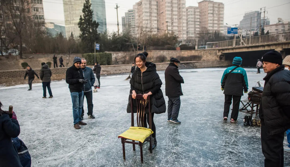 Seorang wanita menggunakan kursi untuk bermain ice skating atau seluncur es di atas sungai yang telah membeku di Beijing, Jumat (1/1). Semenjak membeku, sungai di Beijing ini menjadi objek wisata dadakan yang banyak diminati wisatawan.  (AFP/Fred Dufour)