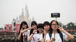 Pengunjung berpose di depan Shanghai Disney Resort di Shanghai, Tiongkok, (16/6). Taman bermain ini dibanjiri pengunjung di hari pertama pembukaan. (AFP Photo/Johannes Eisele)