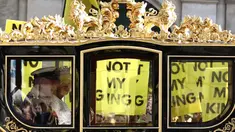 Raja Inggris Charles III dan Ratu Inggris Camilla melakukan perjalanan dengan Diamond Jubilee State Coach melewati para pengunjuk rasa yang memegang plakat "Not My King" dari kelompok anti-monarki Republik saat mereka berdemonstrasi menjelang Pembukaan Parlemen, di seberang Gedung Parlemen di London pada 7 November 2023. (HENRY NICHOLLS/AFP)