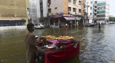 Seorang penjual buah mendorong gerobaknya melintasi jalan yang banjir setelah hujan lebat di Karachi (26/7/2022). Keadaan darurat cuaca diumumkan di Karachi karena hujan muson yang lebih deras dari biasanya terus melanda kota terbesar di Pakistan, membanjiri rumah-rumah dan membuat jalan-jalan tidak dapat dilalui. (AFP/Asif Hassan)