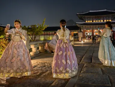 Pengunjung mengenakan gaun tradisional Korea, hanbok sambil berpose saat kunjungan malam ke Istana Gyeongbokgung di Seoul, 4 Oktober 2019. Kunjungan malam tersedia pada minggu ketiga dan keempat setiap bulan mulai dari 26 April sampai 31 Oktober, kecuali pada bulan Agustus. (Photo by Ed JONES / AFP)