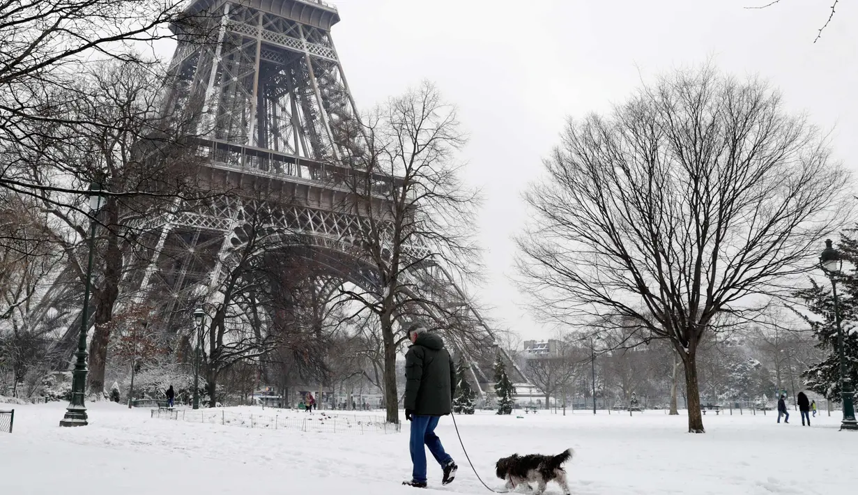 Seorang pria membawa anjingnya berjalan di bawah Menara Eiffel di Paris, Prancis (7/2). Ratusan orang terpaksa meninggalkan mobil mereka untuk tidur di tempat penampungan darurat akibat cuaca ekstrem yang melanda. (AFP Photo / Thomas Samson)