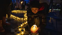 Orang-orang menyalakan lilin membentuk peta Ukraina, untuk mengenang nyawa yang hilang, di depan monumen Taras Shevchenko, di Lviv, Ukraina barat, Selasa malam (5/4/2022). Warga Ukraina berkumpul untuk momen menghormati nyawa yang hilang dalam perang. (AP Photo/Nariman El- Mofty)