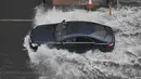 Sebuah mobil melintasi jalan yang banjir saat hujan lebat di distrik The Nine Elms London (25/7/2021). Bus dan mobil terjebak banjir ketika jalan-jalan di London banjir pada hari Minggu, ketika badai petir berulang kali melanda ibu kota Inggris. (AFP/Justin Tallis)