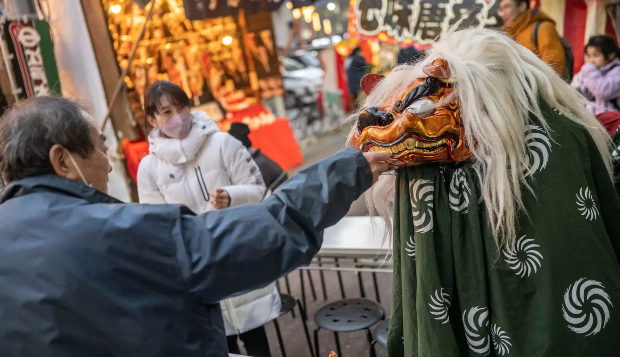 Seorang pria memberikan uang kepada penari singa setelah tampil pada pekan raya akhir tahun di Distrik Nihonbashi, Tokyo, Jepang, 26 Desember 2022. Tak hanya menyuguhkan pemandangan indah dan makanan yang lezat, Jepang juga menjadi negara yang tepat untuk merayakan tahun baru. (Yuichi YAMAZAKI/AFP)