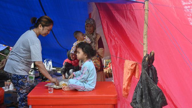Seorang ibu memberi makan putrinya di tenda saat mereka berteduh sementara setelah gempa berkekuatan 6,2 skala Richter pada 15 Januari di Mamuju, Senin (18/1/2021). (AFP/Adek Berry)
