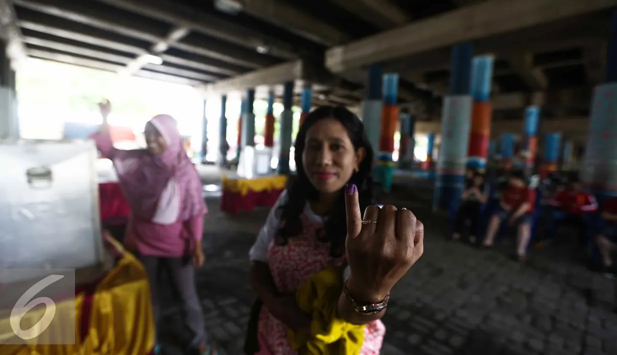 Seorang warga menunjukan jarinya usai menggunakan hak pilihnya dalam Pilkada DKI Jakarta dengan melakukan pencoblosan di TPS 21 di bawah kolong jembatan tol akses Bandara, Petak Asem, Jakarta, Rabu (15/2). (Liputan6.com/Faizal Fanani)