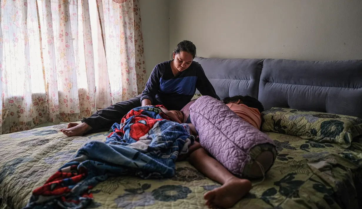 Ibu tunggal Tilda Kalaivani duduk di samping kedua anaknya yang tidur di apartemen sewaannya di Kuala Lumpur pada 6 Juli 2021. Warga Malaysia yang berjuang memenuhi kebutuhan sehari-hari selama pandemi corona yang memburuk, telah mengibarkan bendera putih untuk memohon bantuan. (Mohd RASFAN/AFP)