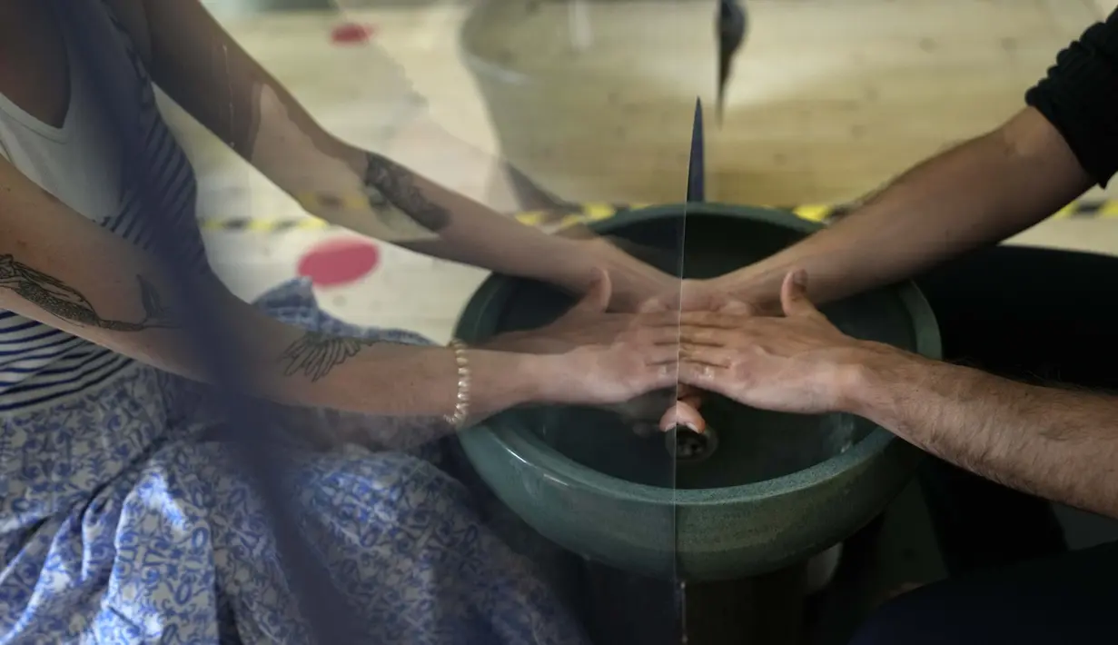 Pengunjung mencoba instalasi 'Cuci Tangan' di pusat budaya Base, di Milan, Italia (15/6/2021). Pertunjukan Cuci Tangan dibuat untuk ritual bagi orang yang lewat dan pengunjung, yang mungkin atau mungkin tidak mengenal satu sama lain, untuk saling berhadapan di sekitar wastafel. (AP Photo/Luca Bruno)