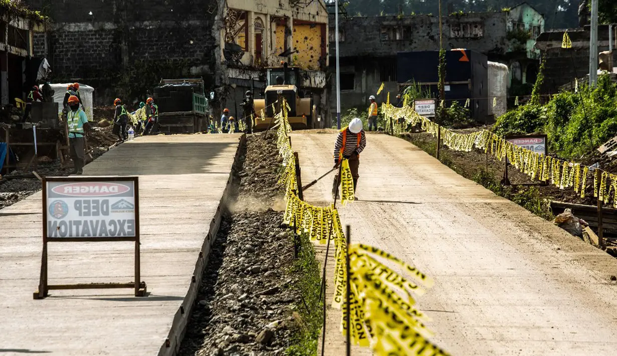 Para pekerja berdiri di sepanjang jalan yang baru diaspal (kiri) empat tahun setelah militan ISIS mengepung Kota Marawi di Mindanao, Filipina, 23 Mei 2021. Lebih dari 1.000 nyawa terenggut dalam pertempuran lima bulan antara pasukan pemerintah dengan militan ISIS. (Ferdinandh CABRERA/AFP)