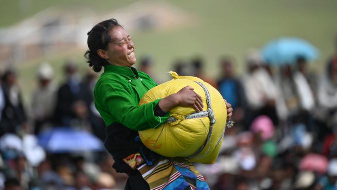 Seorang partisipan mengangkat karung berisi barli dataran tinggi dalam sebuah kompetisi yang digelar saat festival balap kuda Dangjiren di Wilayah Damxung, Daerah Otonom Tibet, China barat daya, pada 11 Agustus 2020. (Xinhua/Purbu Zhaxi)