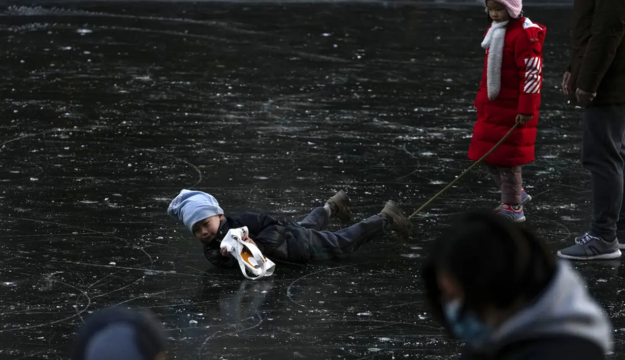 Seorang anak jatuh saat bermain di sungai beku dekat pemukiman warga, Beijing, China, 3 Januari 2022. Libur Tahun Baru dimanfaatkan warga untuk bermain ice skating di sungai dan danau yang membeku. (AP Photo/Andy Wong)
