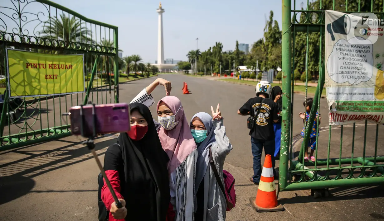 Sejumlah warga berswafoto di depan kawasan Monumen Nasional (Monas), Jakarta, Minggu (26/7/2020). Sejumlah warga mulai mengunjungi kawasan Monas meski masih ditutup sementara di masa PSBB transisi. (Liputan6.com/Faizal Fanani)