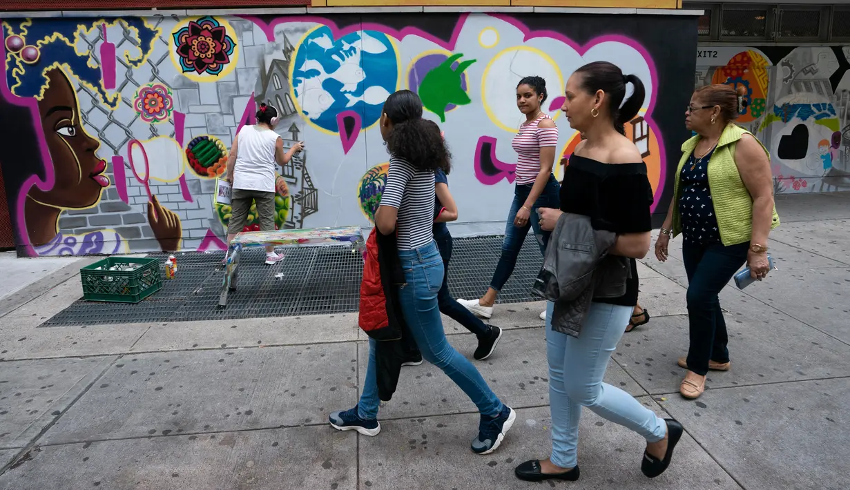 Sekelompok wanita berjalan melewati seniman grafiti Sandra Fabara atau lebih dikenal Lady Pink yang tengah melukis mural di Casita Maria, Bronx, New York, AS, Minggu (2/6/2019). Di usianya yang sudah menginjak 50 tahun, Lady Pink mencari nafkah dengan karya seninya secara legal. (Don Emmert/AFP)