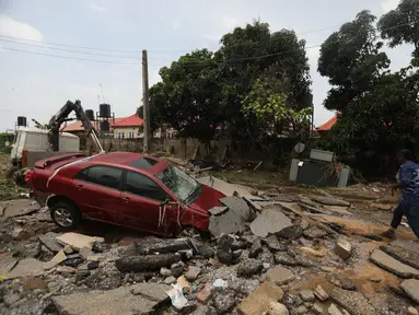 Seorang wanita berjalan melalui jalan yang terkena banjir bandang setelah hujan lebat di Trademoore Estate, Lugbe, Abuja, Nigeria (13/9/2021). Badan Manajemen Darurat Nasional Nigeria (NEMA) mengkonfirmasi 3 orang tewas, dan puluhan mobil dan rumah terkena dampak di malapetaka. (AFP/Kola Sulaimon)