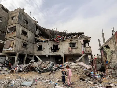 Anak-anak berdiri di luar gedung keluarga Sabah yang terkena serangan udara Israel di Deir el-Balah, Jalur Gaza tengah pada 8 April 2025. (Eyad BABA/AFP)