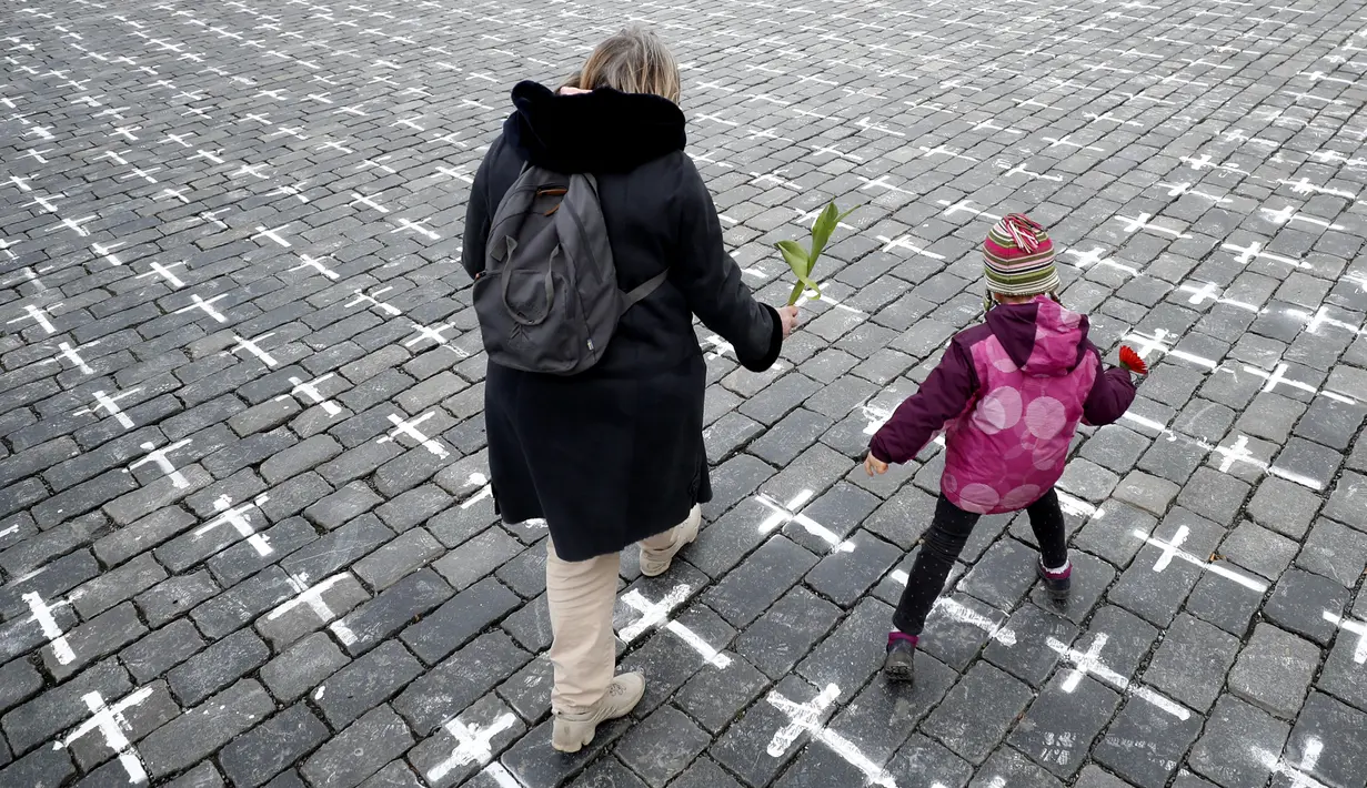 Seorang ibu dan anak membawa bunga saat ribuan salib dilukis di Alun-alun Kota Tua untuk memperingati setahun kematian pasien pertama COVID-19 Ceko, di Praha, Senin (22/3/2021). Pria 95 tahun adalah orang pertama yang meninggal pada 22 Maret 2020 di rumah sakit Bulovka Praha. (AP/Petr David Josek)
