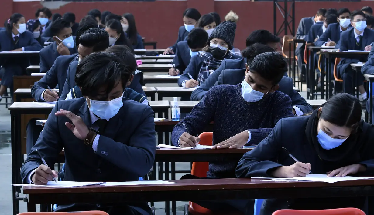 Siswa yang mengenakan masker mengikuti ujian kenaikan kelas XII di lapangan sekolah di Kathmandu, Nepal, Senin (23/11/2020). Nasib sekitar 450.000 siswa kelas XII digantung akibat COVID-19 saat ujian yang dijadwalkan mulai 20 April ditunda karena lockdown pada 24 Maret lalu. (PRAKASH MATHEMA/AFP)