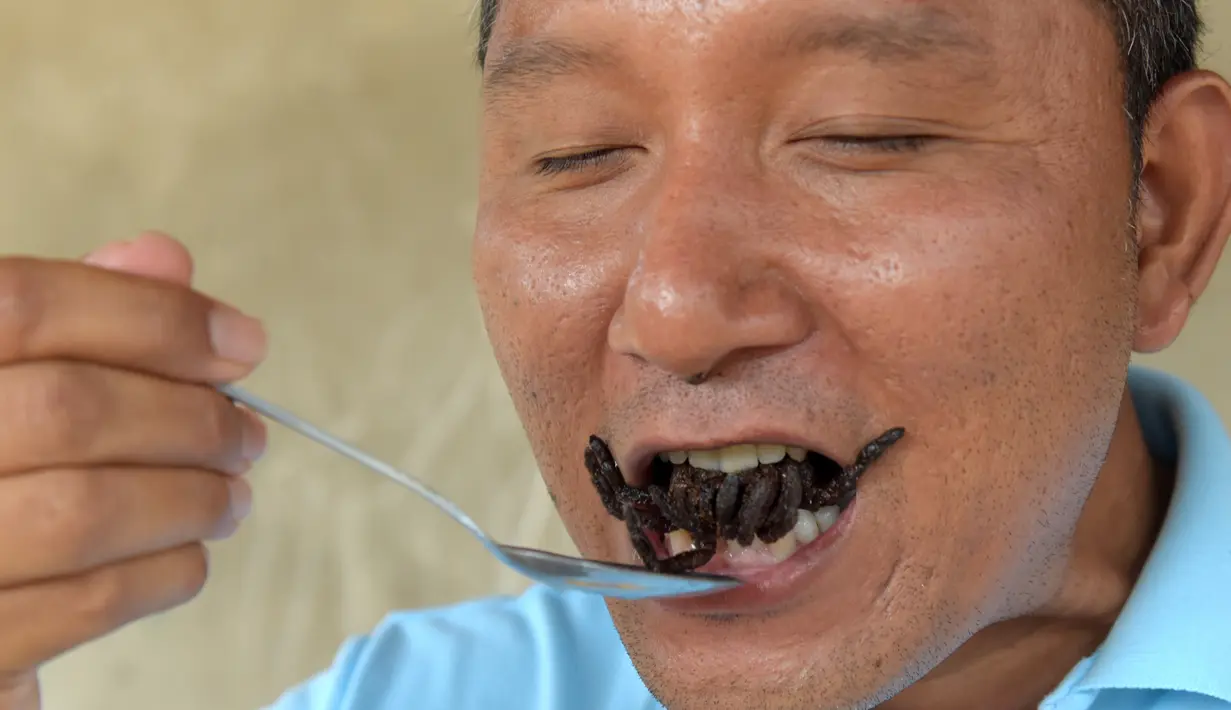 Warga lokal memperlihatkan cara menikmati tarantula goreng di wilayah Skun, Provinsi Kampong Cham, Kamboja, 14 Maret 2018.  Aping, camilan tradisional dari tarantula ini, kian langka sehingga harganya bertambah mahal. (TANG CHHIN Sothy / AFP)