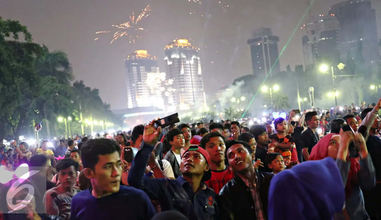 Warga saat menyaksikan pesta kembang api di kawasan Monas, Jakarta, Jumat (1/1). Antusiasme warga yang memadati Monas saat malam pergantian tahun membuat langit di kawasan tersebut dimeriahkan dengan pesta kembang api. (Liputan6.com/Immanuel Antonius)