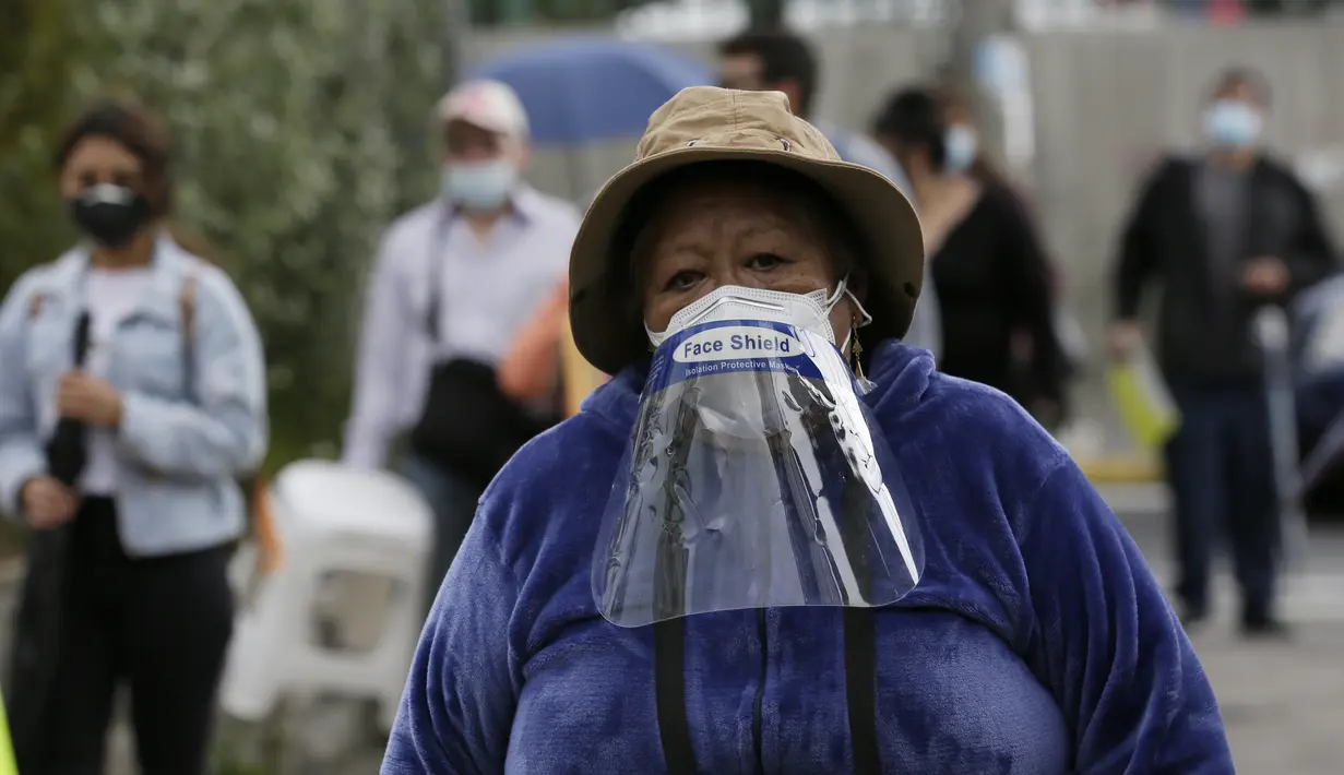 Seorang wanita mengenakan face shield di maskernya bergabung dengan pensiunan untuk disuntik vaksin Covid-19 di luar pusat vaksinasi Social Security Institute di Quito, Ekuador, Kamis (6/5/2021). Para lansia dan pendampingnya menunggu berjam-jam untuk divaksinasi. (AP Photo/Dolores Ochoa)