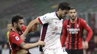 Gelandang AC Milan, Hakan Calhanoglu berebut bola dengan bek Cagliari, Luca Ceppitelli pada pekan ke-37 Serie A di San Siro, Senin (17/5/2021) dini hari WIB.  AC Milan gagal menjauh di klasemen Liga Italia usai imbang 0-0 lawan Cagliari. (AP Photo/Luca Bruno)