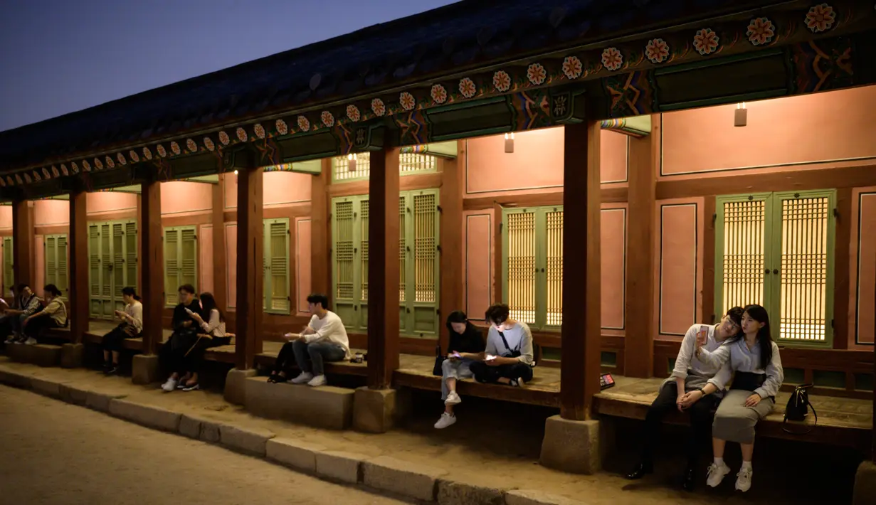 Gambar pada 4 Oktober 2019, wisatawan duduk di bangku dekat halaman saat kunjungan malam ke Istana Gyeongbokgung di Seoul, Korea Selatan. Kunjungan malam tersedia pada minggu ketiga dan keempat setiap bulan mulai dari 26 April sampai 31 Oktober, kecuali pada bulan Agustus. (Photo by Ed JONES / AFP)