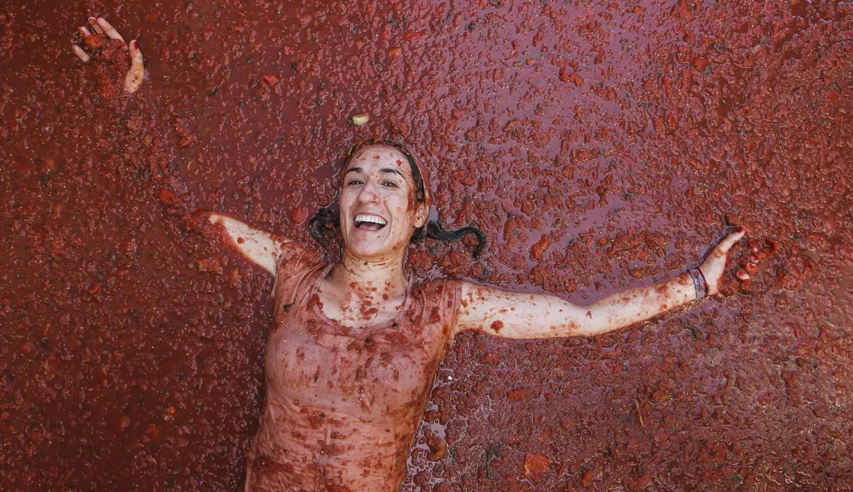 Seorang peserta berbaring di genangan tomat yang tergencet selama "Tomatina" tahunan, pesta pertarungan tomat di desa Bunol dekat Valencia, Spanyol, Rabu (31/8/2022). La Tomatina adalah festival lempar tomat Spanyol yang berlangsung setiap tahun pada hari Rabu terakhir bulan Agustus. (AP Photo/Alberto Saiz)