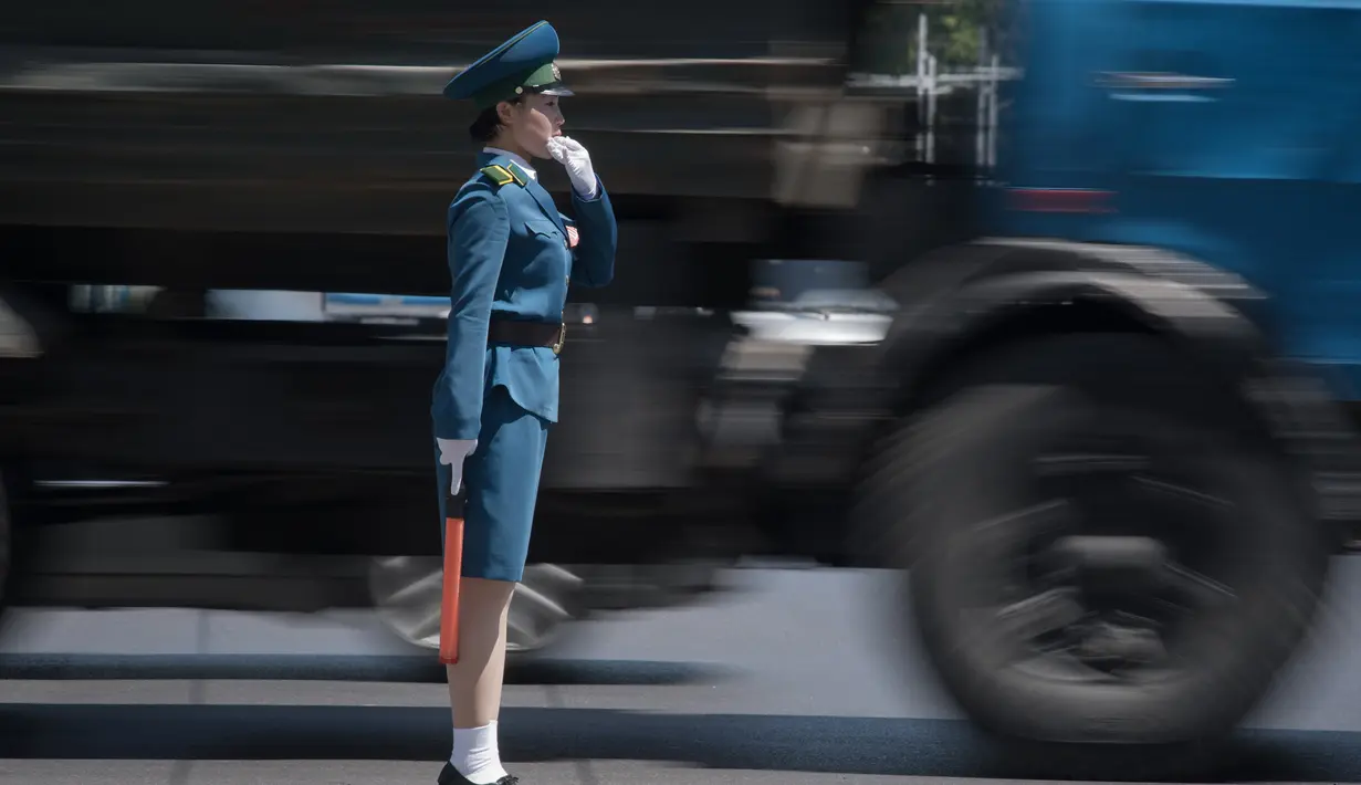 Seorang polisi wanita mengatur lalu lintas di sebelah truk yang melintas di Pyongyang, Korea Utara (5/6). Para polisi wanita ini harus meninggalkan profesi mereka jika mereka menikah dan akan pensiun ketika memasuki usia 26 tahun. (AFP Photo/Ed Jones)