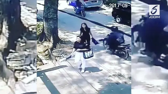 Seorang wanita yang sedang berjalan kaki dijambret oleh seorang pengendara motor. Kejadian ini terekam CCTV sebuah gedung.