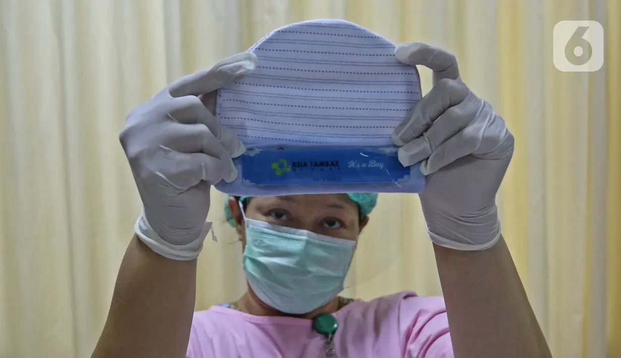 Perawat kamar bayi menunjukkan face shield (italic) di  RSIA Tambak, Jakarta, Selasa (14/4/2020). RSIA Tambak membuat face shield (italic) mandiri menggunakan plastik mika, direkatkan dengan karet atau bandana menggunakan topi bayi menghindarkan alergi pada kulit bayi. (Liputan6.com/Herman Zakharia)