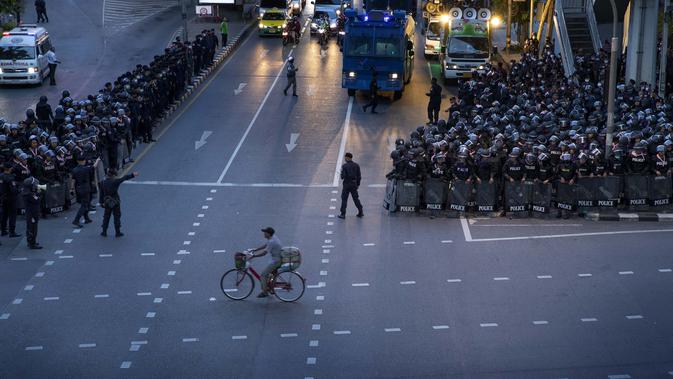 DEMONSTRASI DI THAILAND: Seorang pria mengendarai sepedanya melewati polisi antihuru-hara yang mengambil posisi di persimpangan menuju Gedung Pemerintah setelah mengejar sekelompok kecil demonstran pro-demokrasi di Bangkok, Thailand, Kamis (15/10/2020). (AP Photo/Gemunu Amarasinghe)