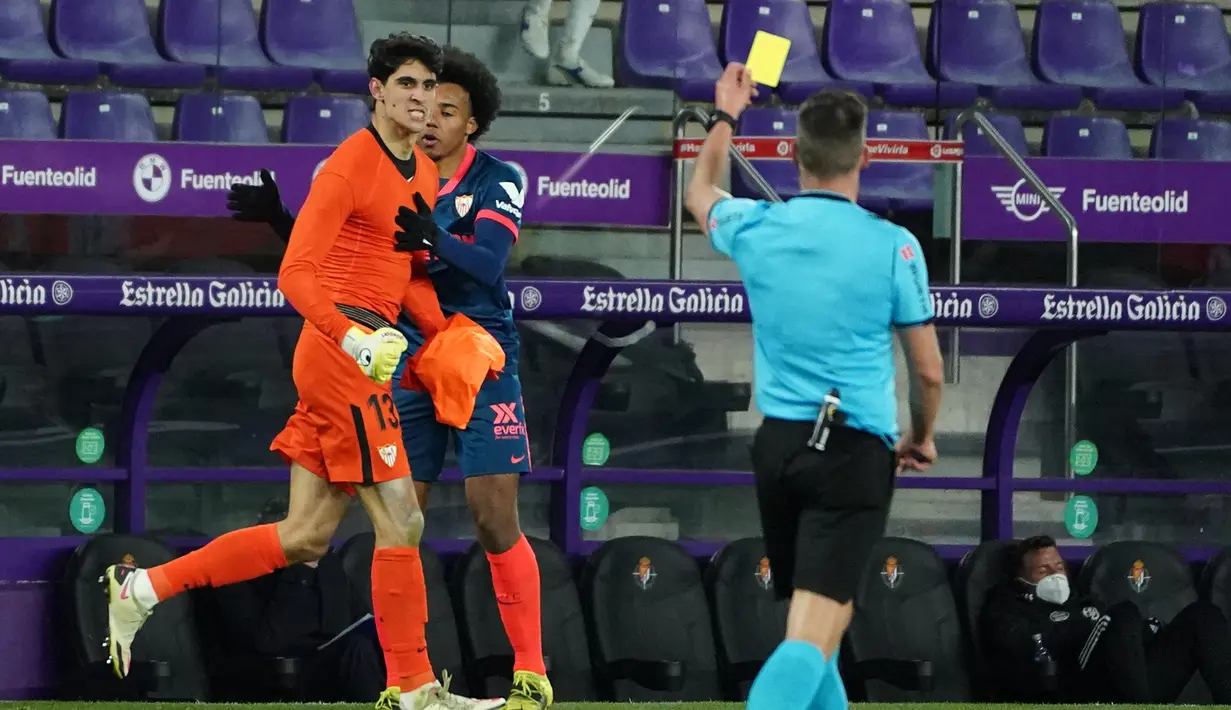 Kiper Sevilla, Yassine Bounou Bono (kiri) menerima kartu kuning dari wasit Adrian Cordero saat menghadapi Real Valladolid dalam laga lanjutan Liga Spanyol 2020/2021 pekan ke-28 di Jose Zorrilla Stadium, Valladolid, Sabtu (20/3/2021). Sevilla bermain imbang 1-1 dengan Valladolid. (AFP/Cesar Manso)