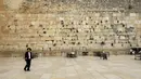 Seorang lelaki Yahudi ultra-Ortodoks berjalan di sebelah Tembok Ratapan yang hampir kosong, situs paling suci di mana orang Yahudi dapat berdoa sebagai bagian dari langkah-langkah untuk mencegah penyebaran Covid-19 di Kota Tua Yerusalem (31/3/2020). (AFP/Emmanuel Dunand)