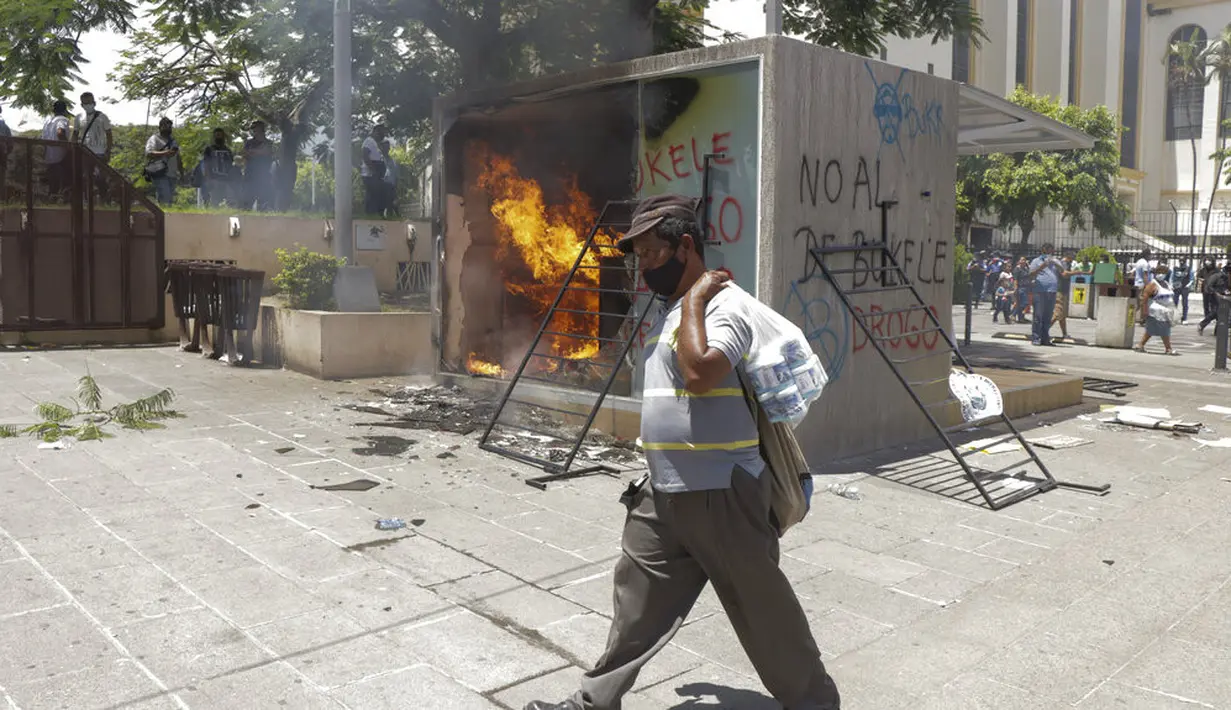 Seorang pria melintasi mesin ATM bitcoin bernama Chivo yang dibakar dalam protes terhadap Presiden Nayib Bukele di San Salvador, El Salvador, Rabu (15/9/2021). Ribuan warga Salvador berdemonstrasi menentang bitcoin, yang disahkan sebagai alat pembayaran oleh pemerintah. (AP Photo/Ivan Manzano)
