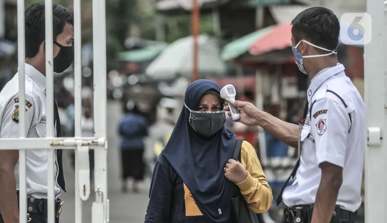 Petugas keamanan memeriksa suhu tubuh orangtua dari anak penerima KJP sebelum memasuki area pengambilan kartu di kawasan Matraman, Jakarta, Selasa (24/11/2020). (merdeka.com/Iqbal S. Nugroho)