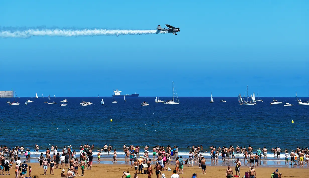 Pesawat Cessna L19 Bird Dog bermanuver di atas Pantai San Lorenzo di Gijon, Spanyol, Minggu (24/7). Para pengunjung pantai terlihat menikmati pertunjukan tersebut. (REUTERS/Eloy Alonso)